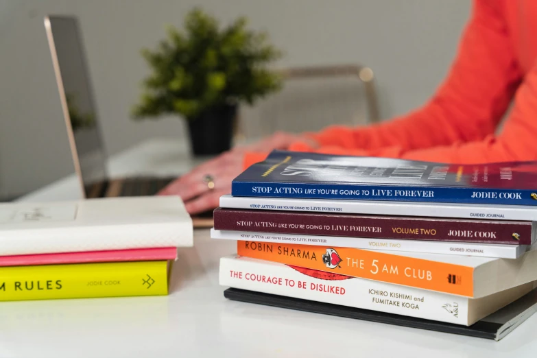 stacked books sitting next to a laptop computer on a desk