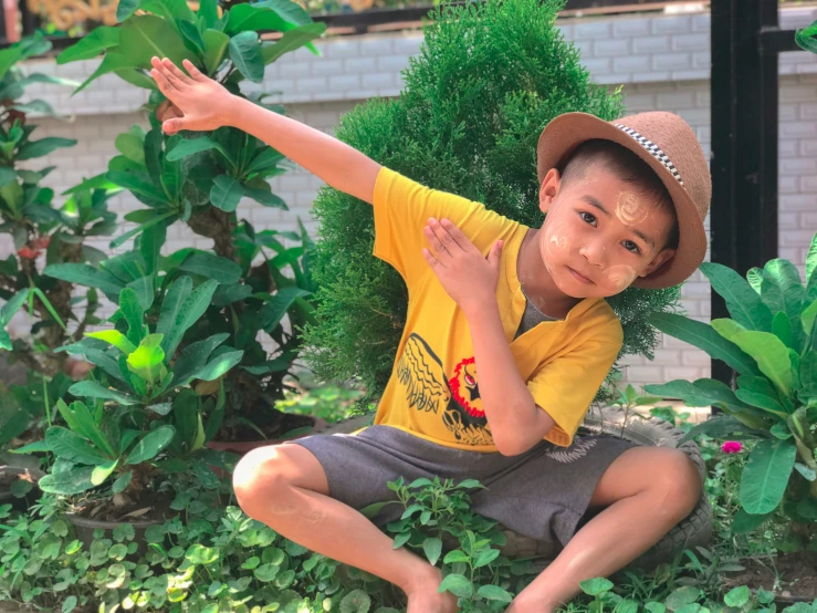 a boy in a hat is sitting on the ground with his arms raised