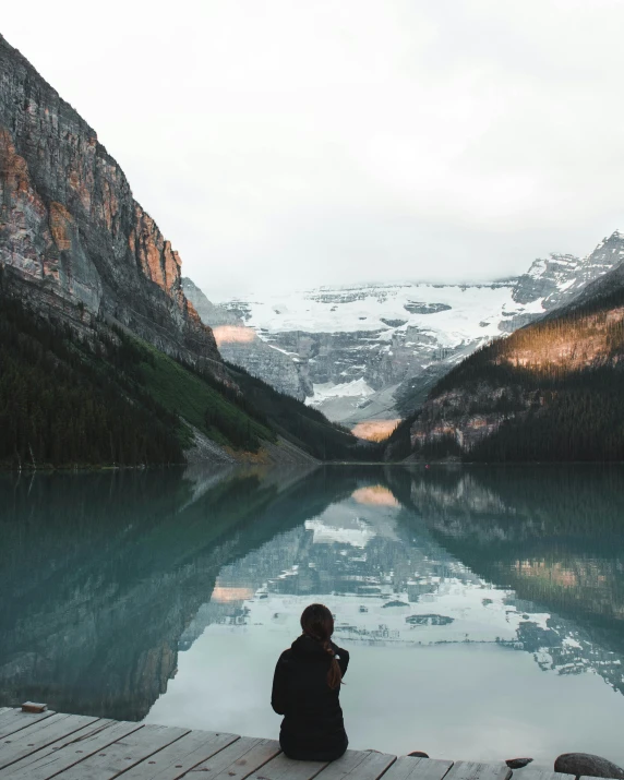 a person sits on a dock in front of a mountain