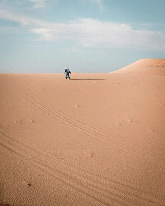 a man walks across a large sand dune