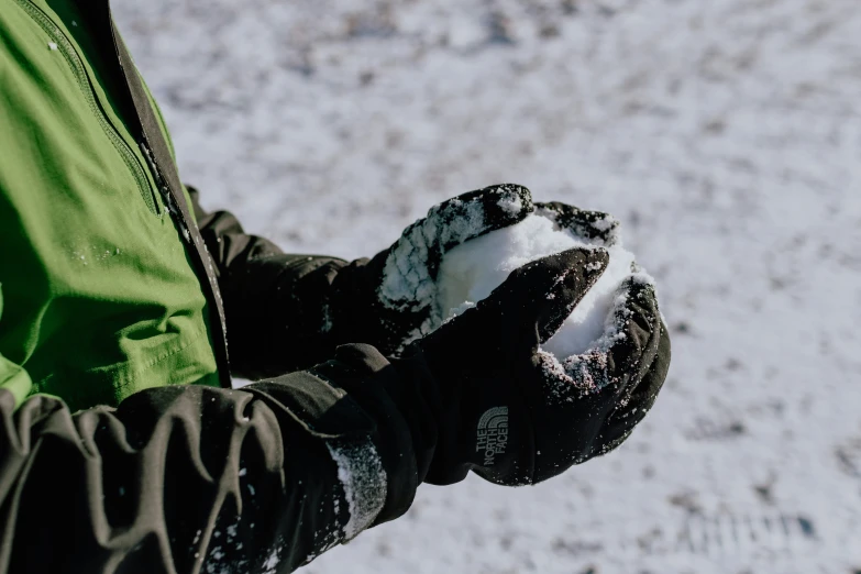 a person wearing some gloves with a snowball in their hand