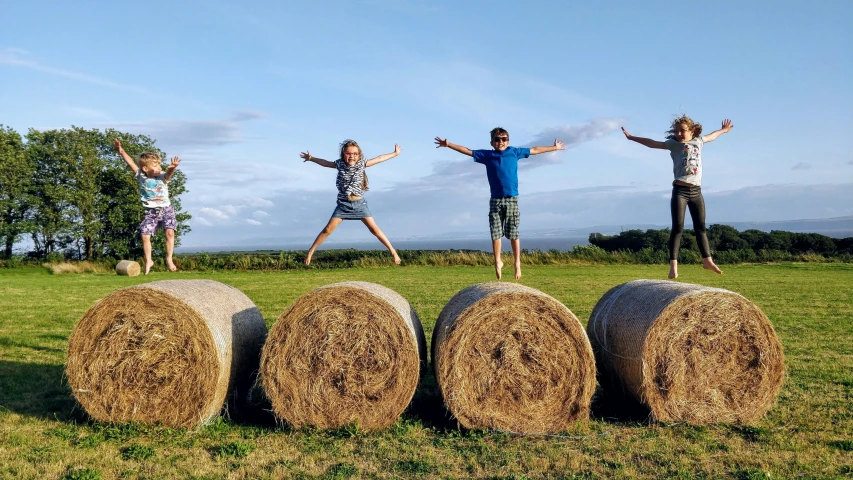 three people jumping over hay bales in a field