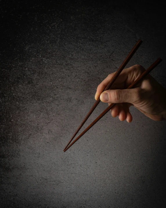 two chopsticks held up by a hand with dark background