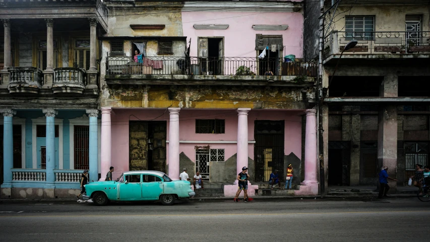 a green car parked in front of a tall pink building