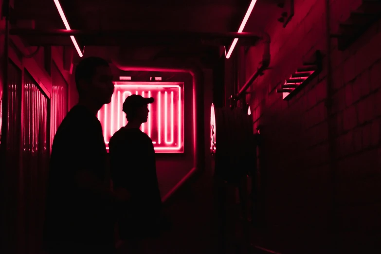 two people standing in an enclosed walkway near neon lights