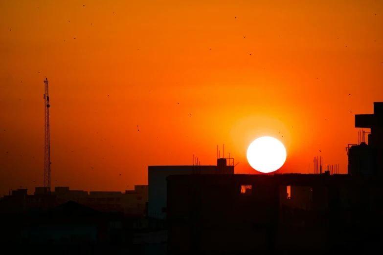 the sun sets behind silhouettes buildings in the city