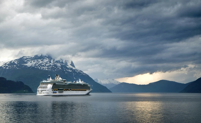 a cruise ship anchored in the ocean with mountains on the far side