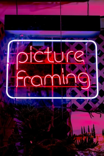 a neon sign reads picture framing on a street corner