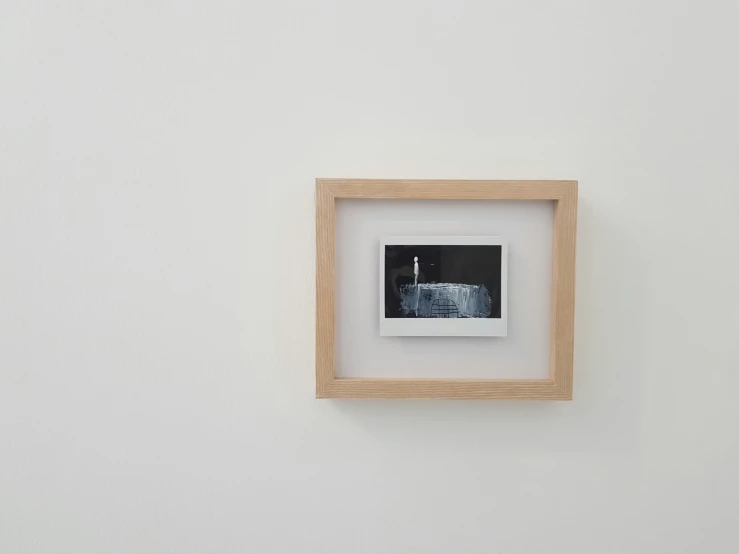 a small white square frame hangs on the wall of an art gallery