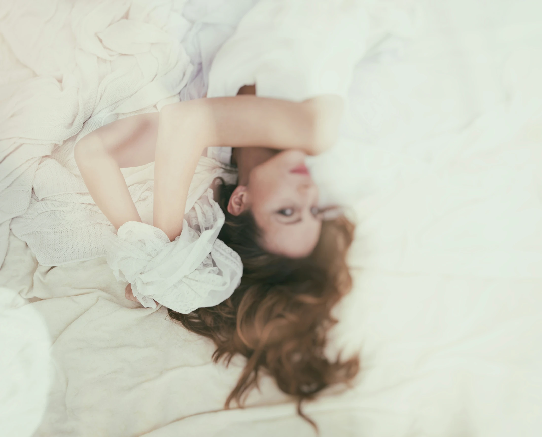 a woman laying in bed on top of a white blanket