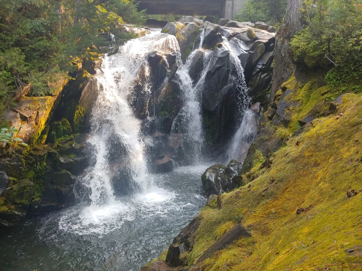 a waterfall near a road and bridge near trees