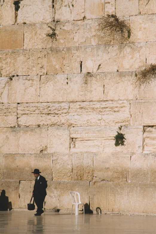 a man with a hat and a cane in front of a large stone wall