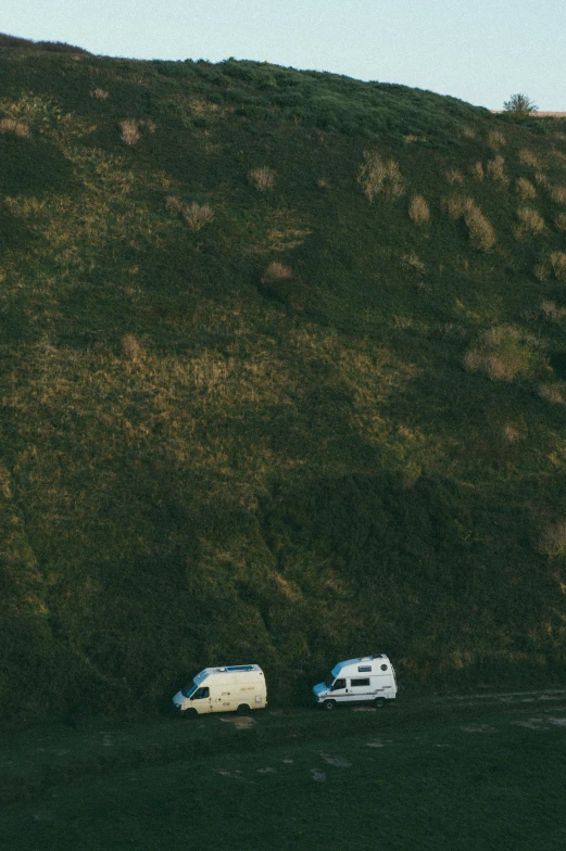 two white vans on grass next to a hill