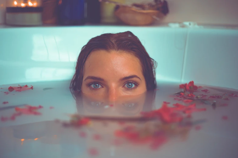 a woman sits in a tub with petals all over the surface