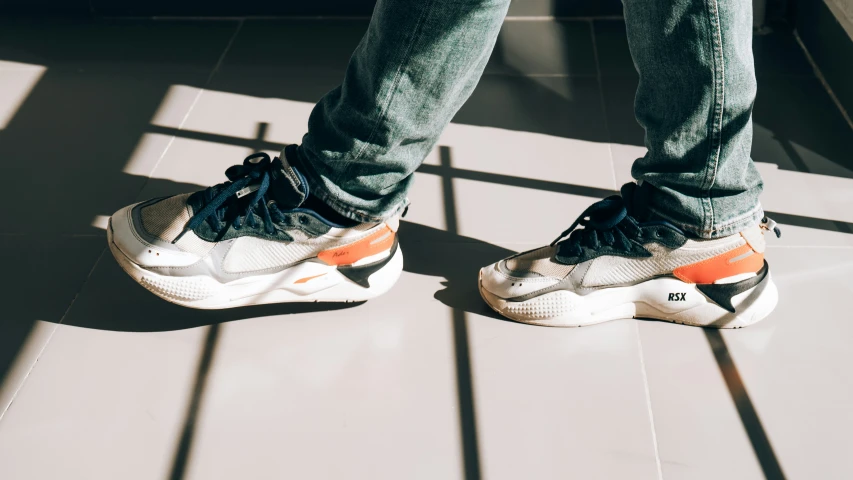 a person wearing grey jeans and orange sneakers standing on the floor