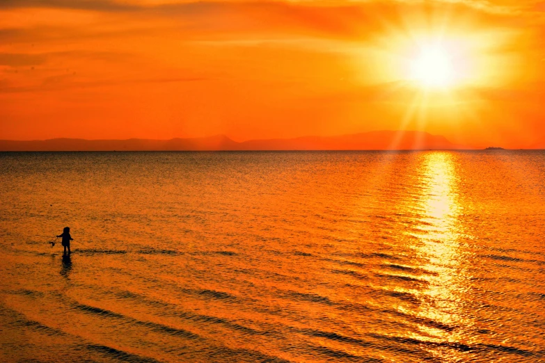 a man wades out in the middle of a large body of water as the sun rises