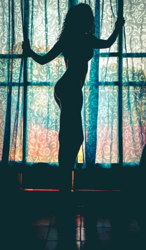 a woman in silhouette stands against a window