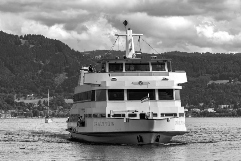 a ferry boat coming down the river with a hill behind it