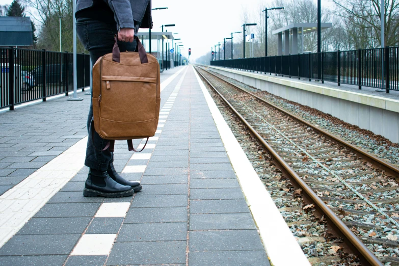 a person with a brown briefcase stands on railroad tracks