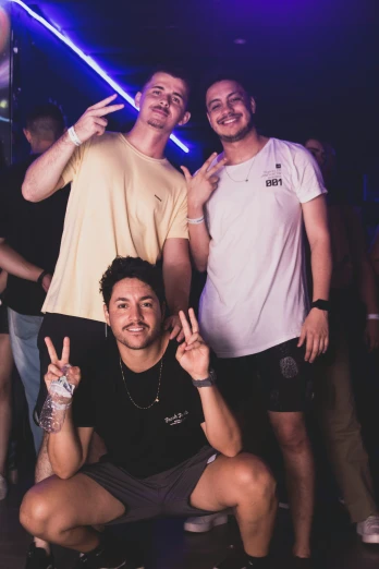 three young men posing for the camera with one of them giving a peace sign