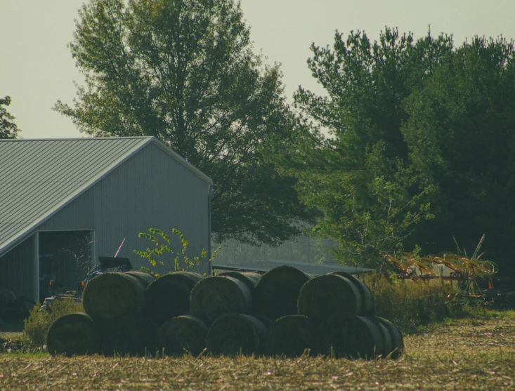 hay bails stacked next to a barn and tree