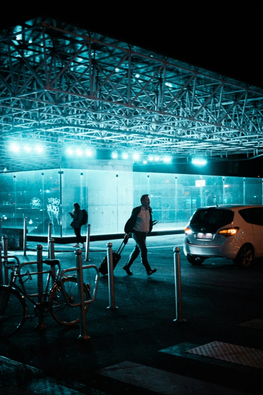 two people walking on the side of a street at night with lights