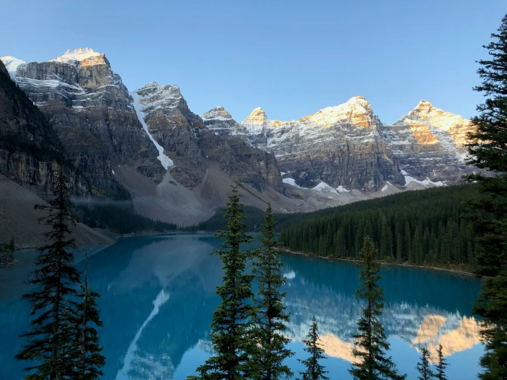 mountains rise above a small lake that is reflecting the snow - capped peaks in the foreground