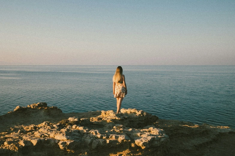 a woman looking out at the ocean, from a cliff