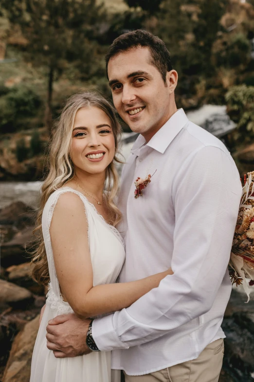 an attractive young blonde couple posing for a pograph near the rocky river