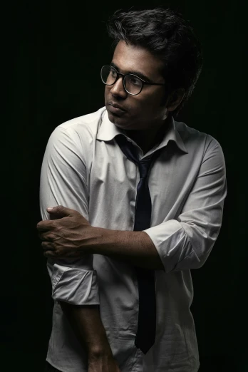 man wearing glasses, black tie, and shirt and folded arms in a studio s