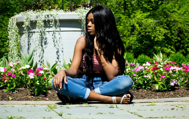 an african american woman sitting on the ground in front of flowers