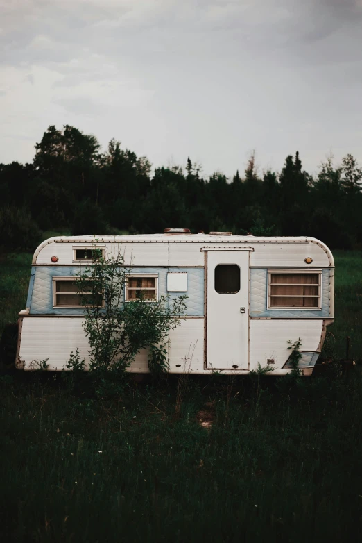 a small, dilapidated travel trailer with weeds in the grass