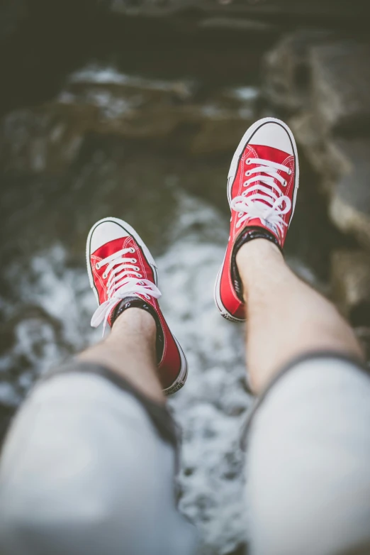 someone wearing red sneakers standing on some rocks near the water