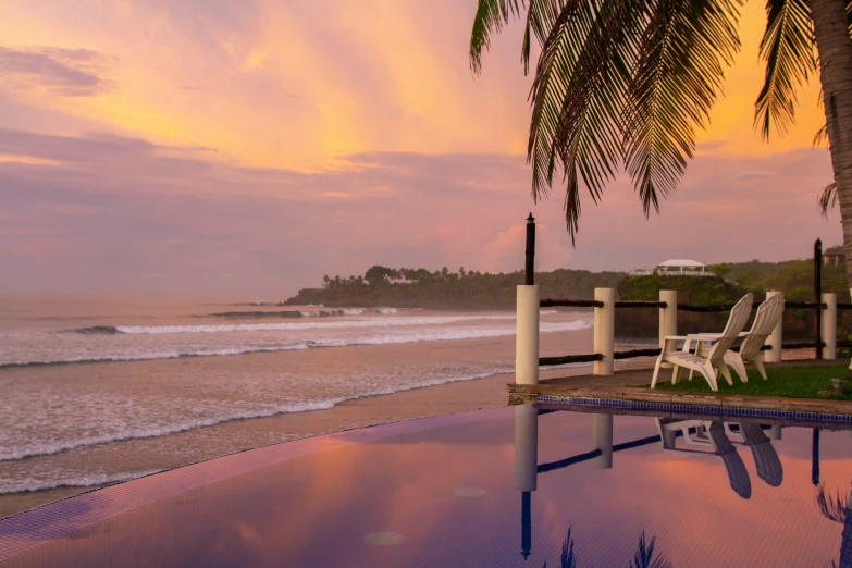 lounge chairs sit on a pier next to a body of water at sunset