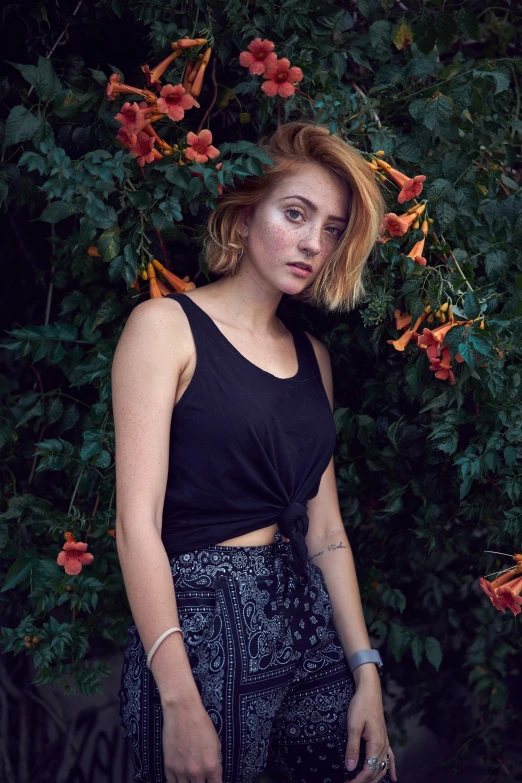 a young woman stands in front of a flowered bush