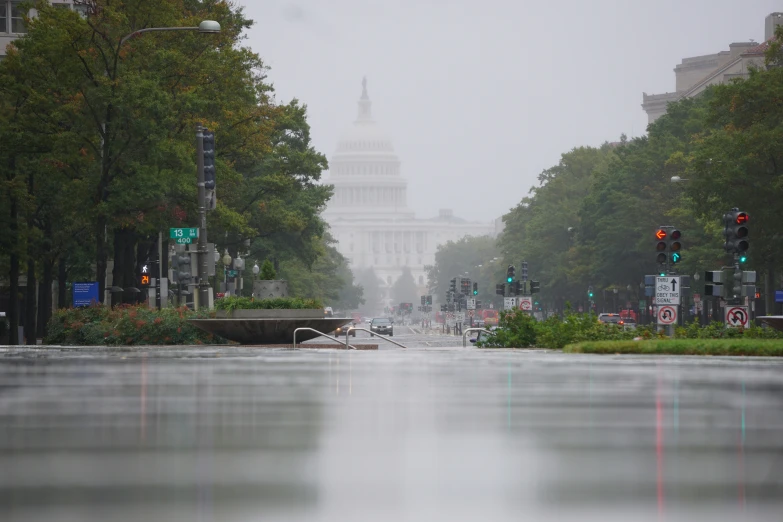 an umbrella stands above a wet street as traffic drives by in front of the us capitol building