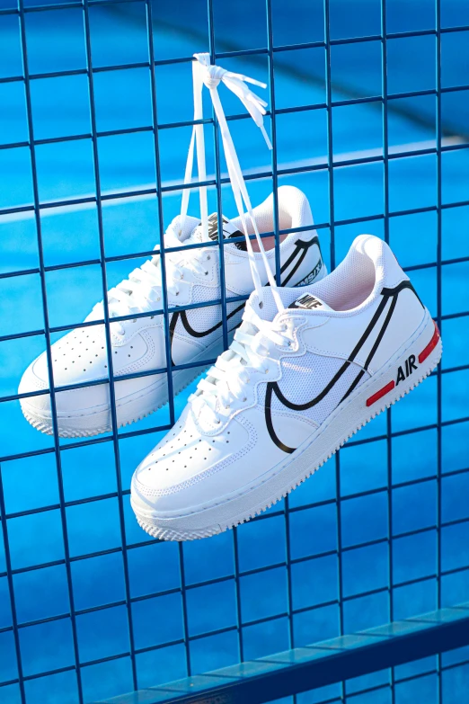 a pair of white nike tennis shoes are hanging on a blue fence