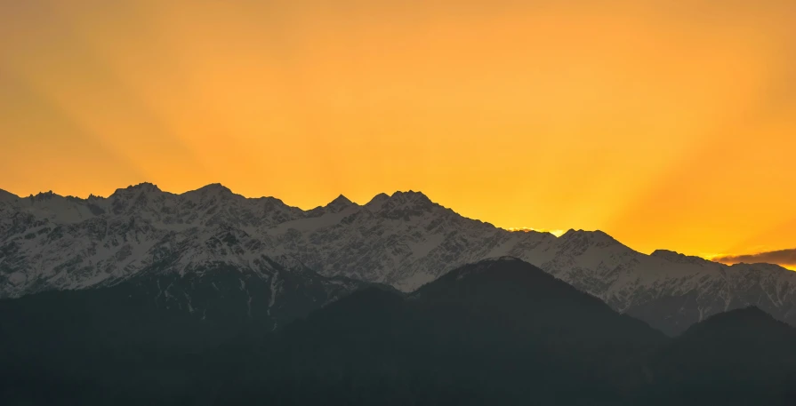 the sun is setting behind some tall mountain tops