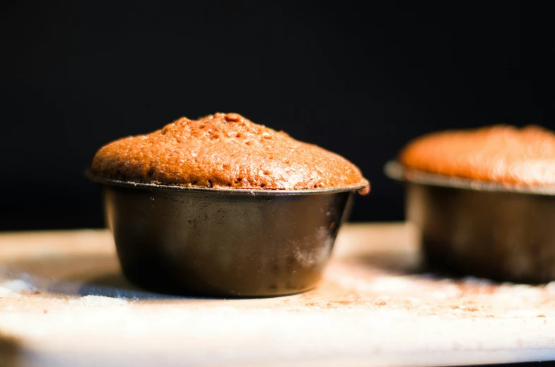 two muffins in small cups with a spoon sitting on the bottom