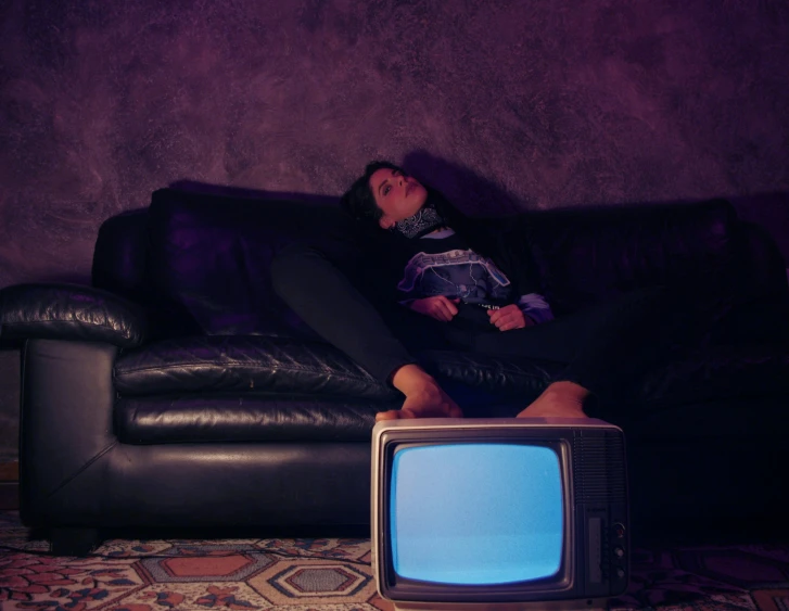 a woman laying on a couch in front of an old television