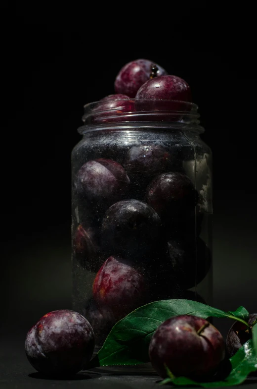 a glass jar filled with some plums on top of a table