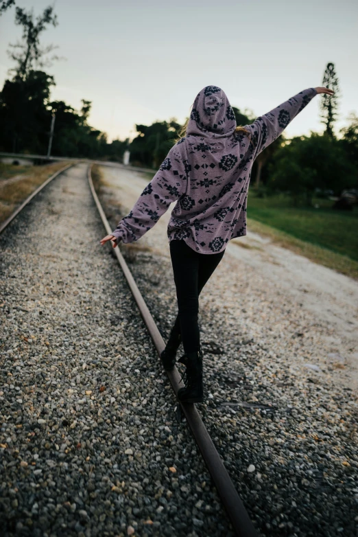 a woman in a jacket walking on a railroad track