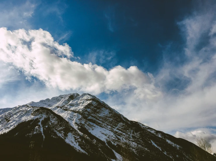 clouds are floating over a snow - capped mountain