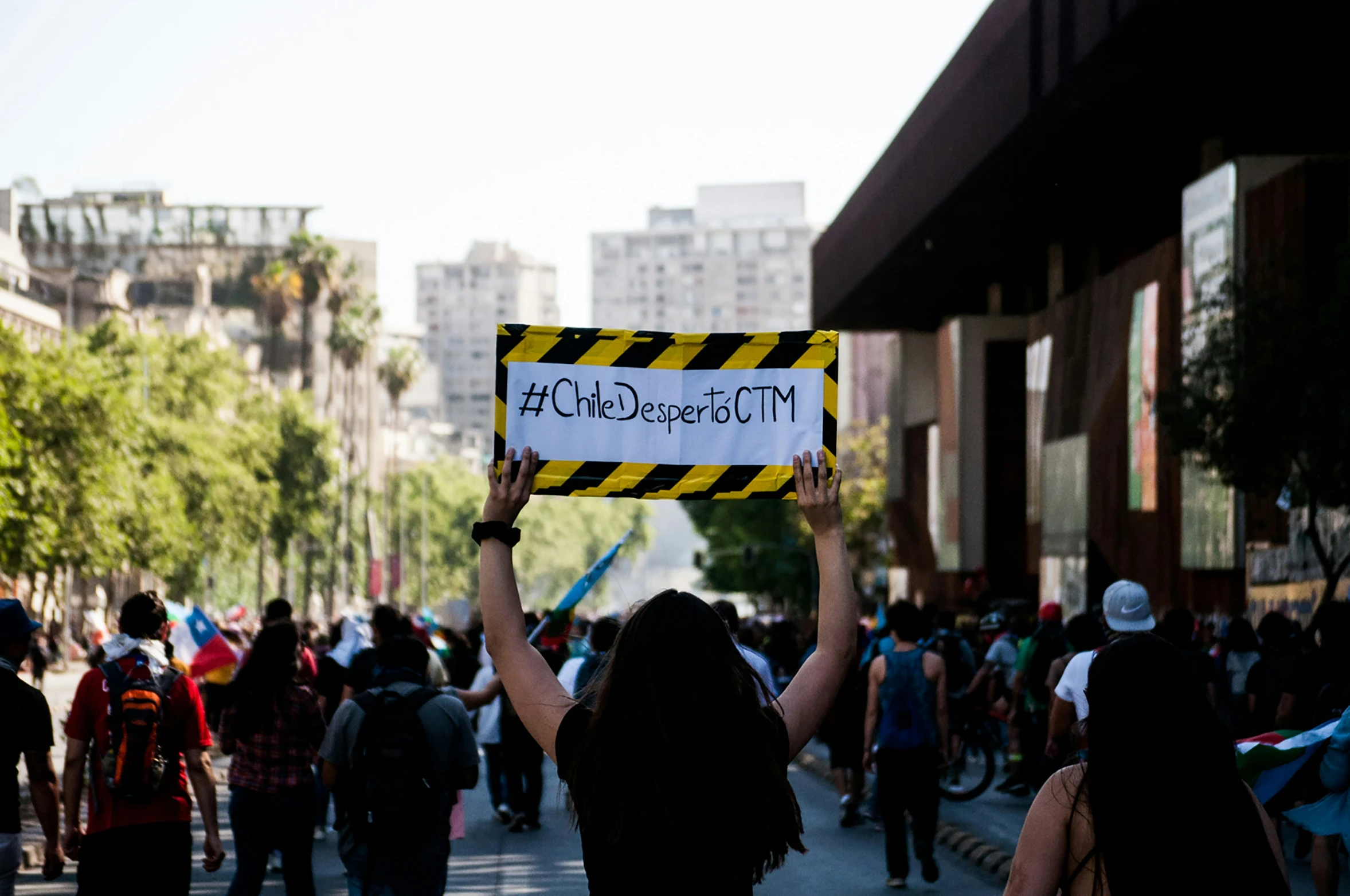 a woman holding a sign with a yellow and black warning strip on it in the middle of a crowd