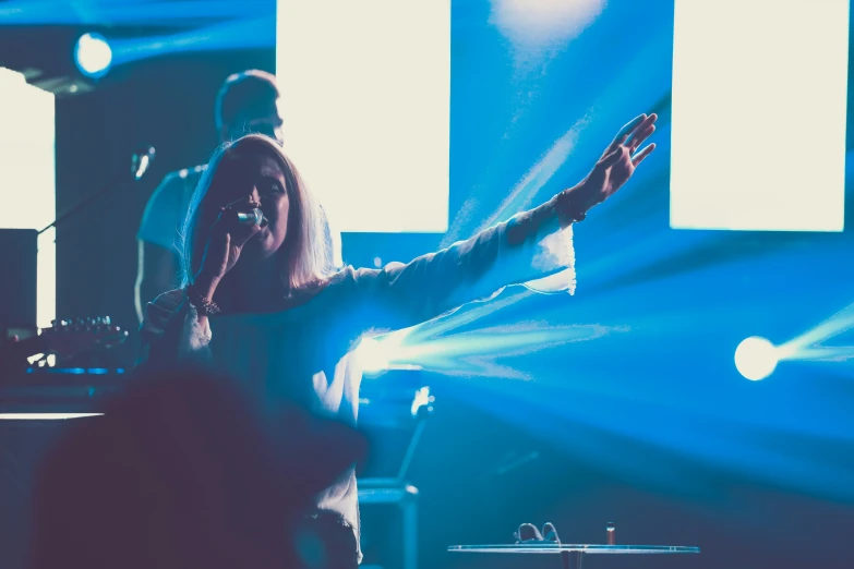 woman with hands raised at microphone on stage