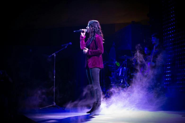 a woman is standing on stage singing with smoke behind her