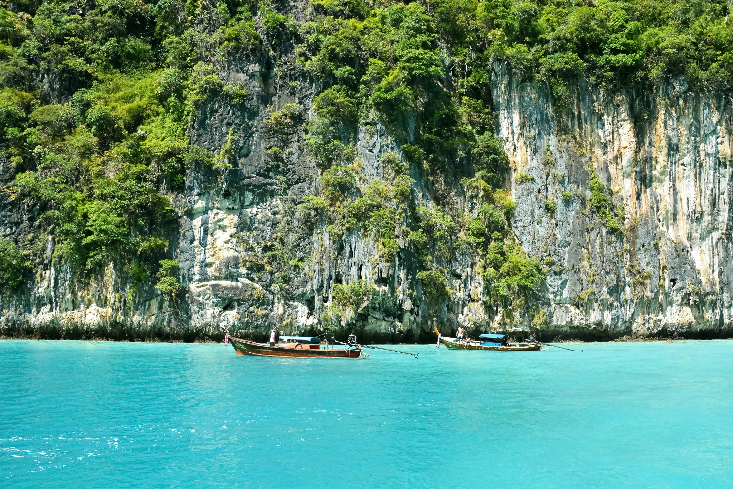 several boats sit in the water near a cliff face