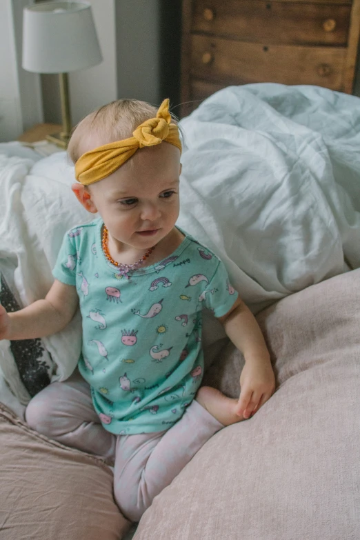 a baby with a big bow is sitting on a bed