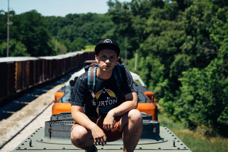 a man wearing a backpack sitting on a track next to train