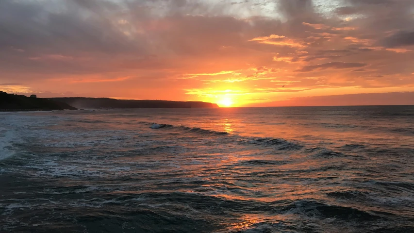 the sun sets behind a lone tree covered hill on a sandy shore